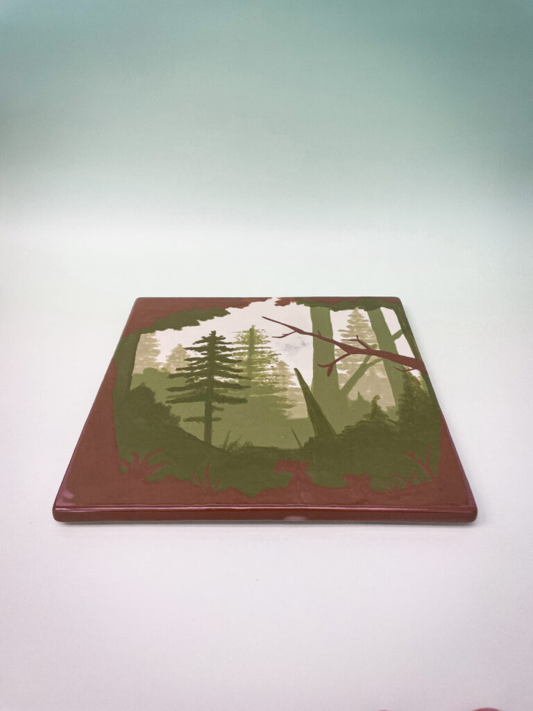 A ceramic tile displayed at an angle, featuring a serene forest scene with tall trees and mist in shades of green and brown against a smooth gradient background.
