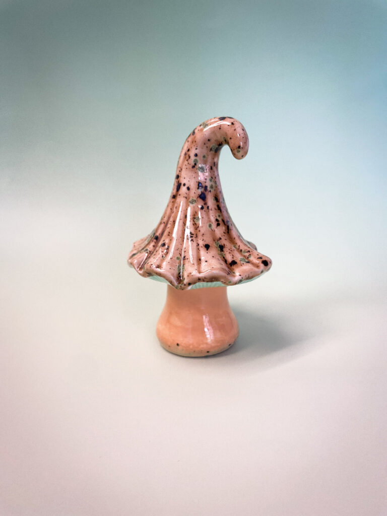 A whimsical, handcrafted ceramic mushroom with a speckled brown cap and a curly top, set against a soft, mint-green background.