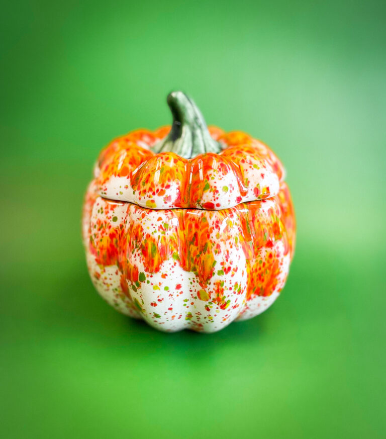A ceramic pumpkin-shaped container with an orange and green speckled pattern against a vibrant green background.
