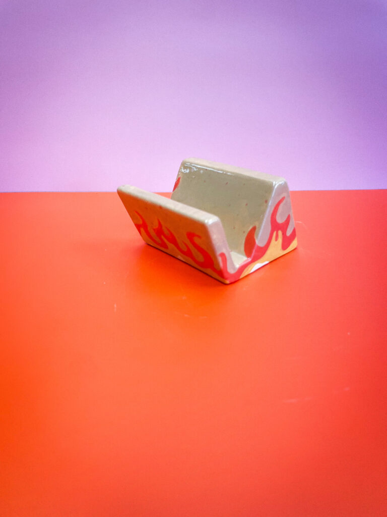 A ceramic phone stand with a red flame design rests on a red and purple gradient background.