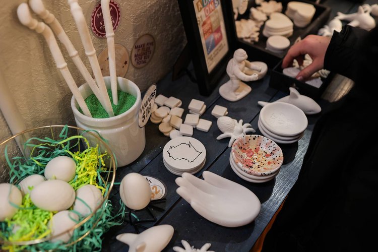 A variety of ceramic items are displayed on a table, featuring eggs, whales, hands, and a bird sculpture. In Superior, Wisconsin, where fun things to do abound, someone reaches for a black dish amid colorful shredded paper in a bowl and other decorative pieces.