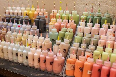 Rows of small bottles filled with various pastel and bright-colored liquids, each labeled with numbers and equipped with pointed nozzle caps, are arranged in tiers on a shelf, reminiscent of the vibrant art scenes in Duluth, MN and Superior, Wisconsin in the Twin Ports region.