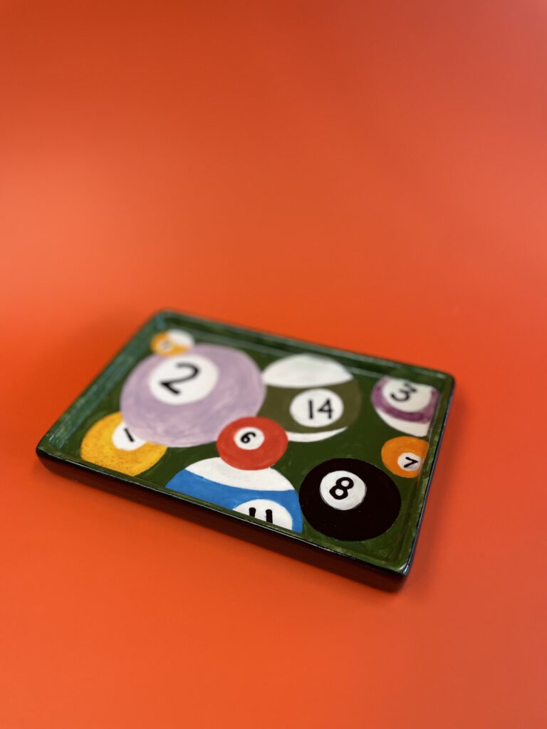 Rectangular ceramic plate on an orange surface, featuring a vibrant design of colorful billiard balls with numbers.